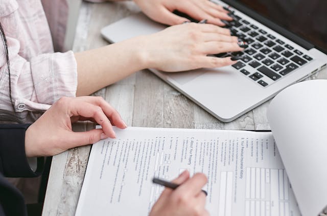 Person typing on computer while someone signs documents