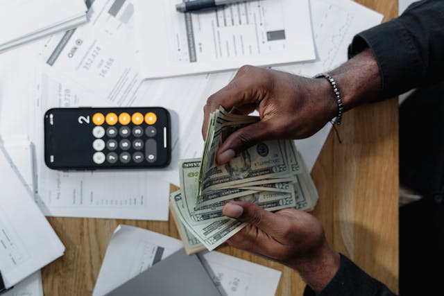 person counting money over documents and a calculator