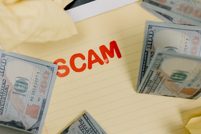 The word scam in red on a yellow notepad surrounded by money